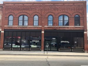Photo of the outside of Hendricks. The store front is red brick with big windows and black window casings. There is a parking meter in front of the door.