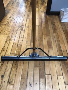 Photo of Squeegee with metal top and rubber bottom resting on wood floor.