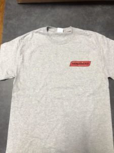 Photo of gray Hendricks T-shirt with red Hendricks logo in corner and black outline.